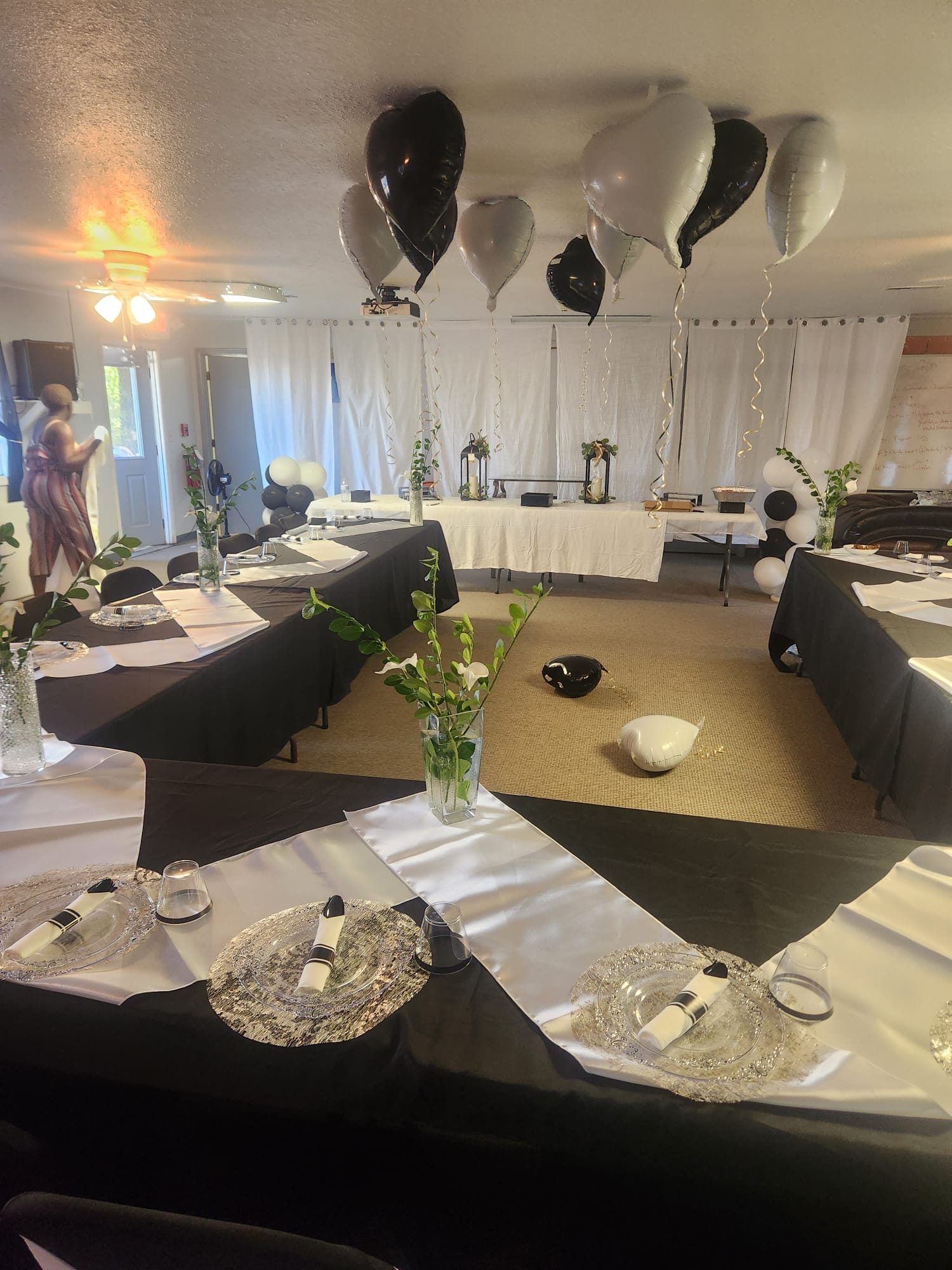 Black and white formal banquet tables with satin runners, charger plates, greenery, and heart balloons