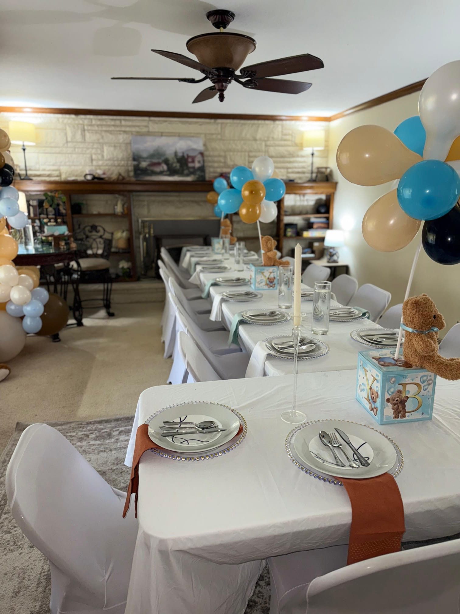 Teddy-bear themed guest tables with white linens, blue block centerpieces, and a stone fireplace beyond